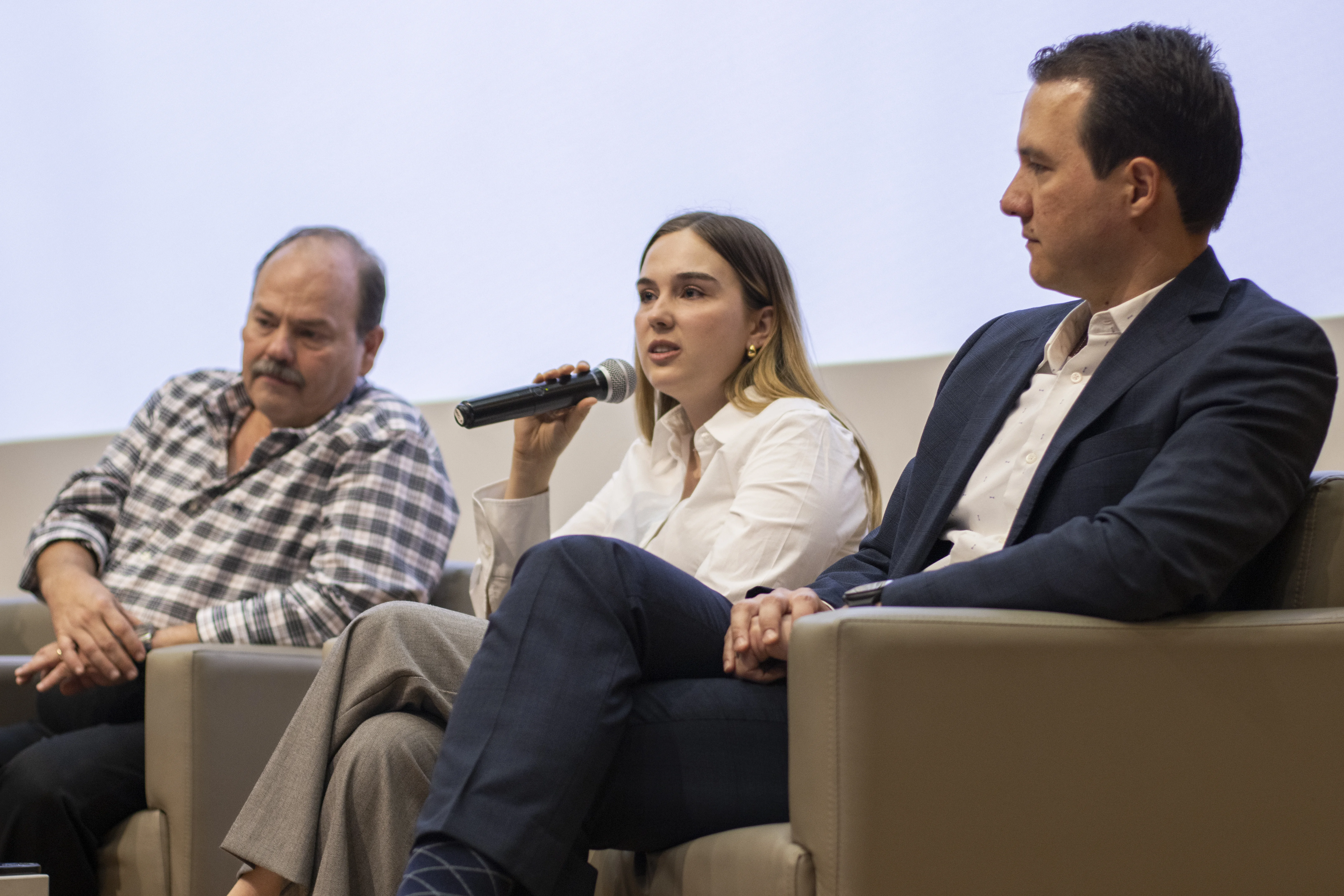 Estudiante interviene con micrófono durante un panel académico de la FLDM, junto a dos ponentes
